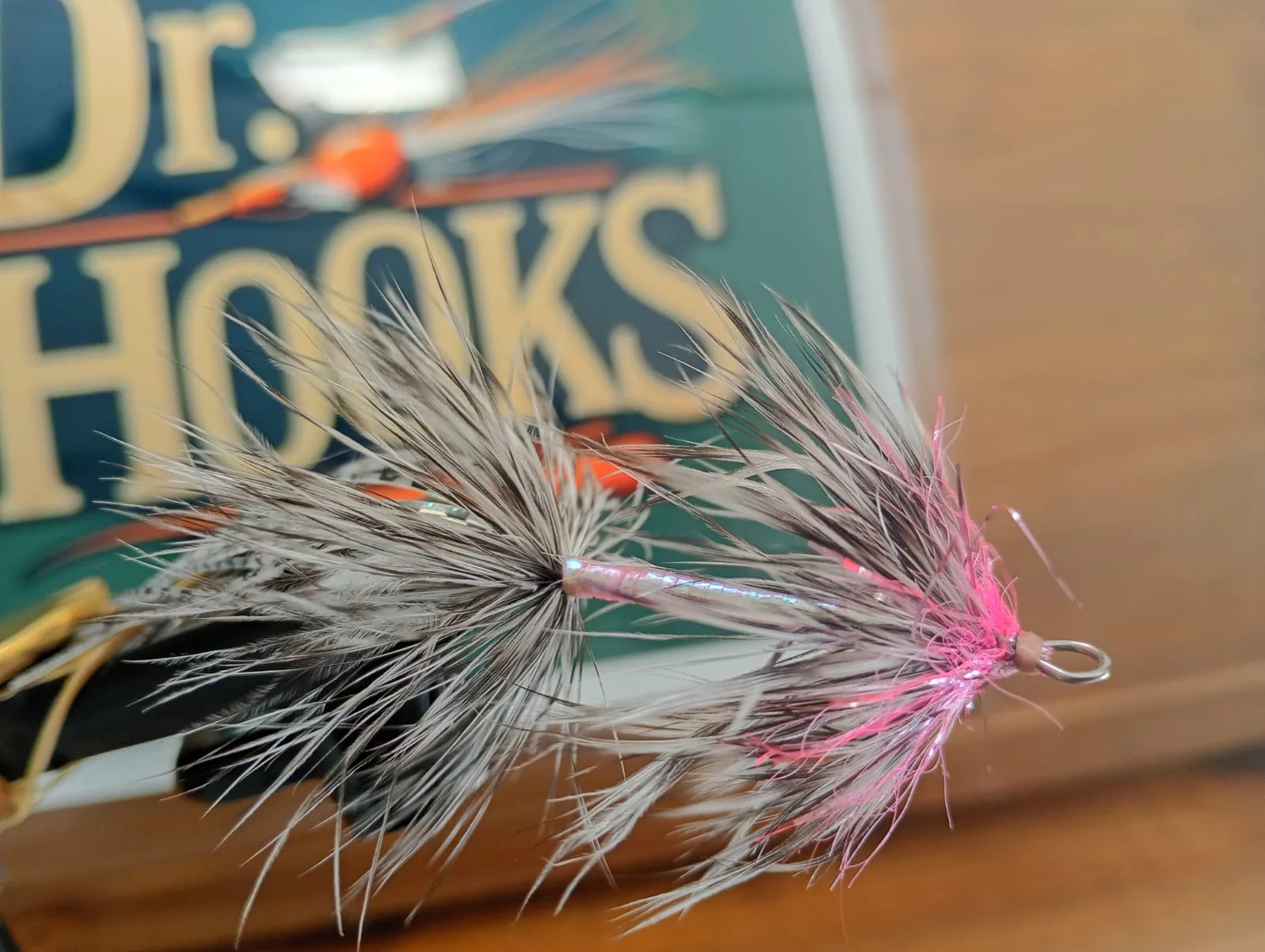 Streamer de plumas grises y cuerpo rosa atado por Dr. Hooks, delante del cartel de la marca